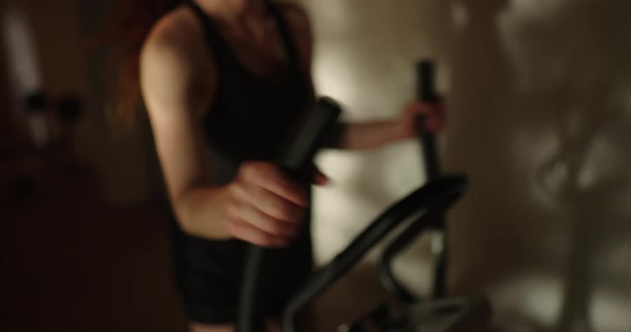 Woman with black tank top and shorts uses cross trainer in gym