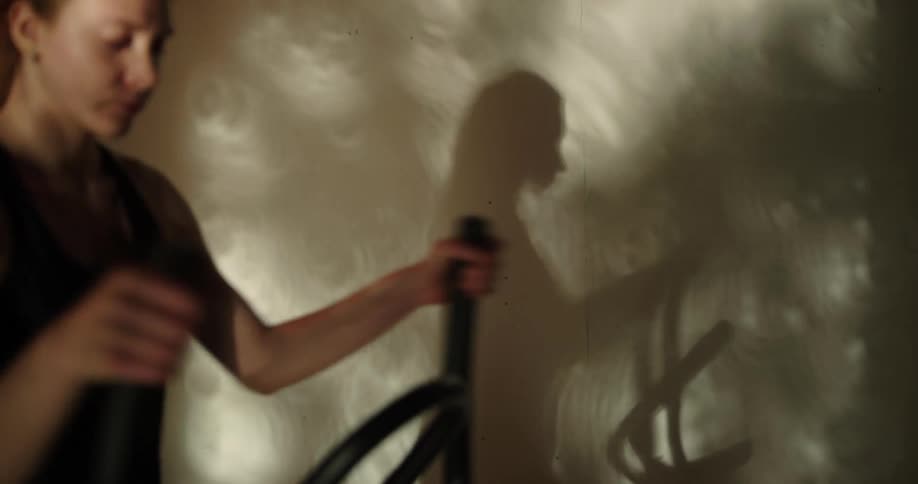 Redhaired woman exercises on elliptical casting a shadow onto a nearby wall