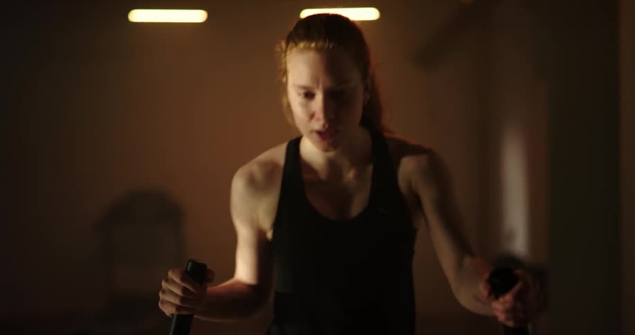 Redhead exercises on elliptical machine in dim room