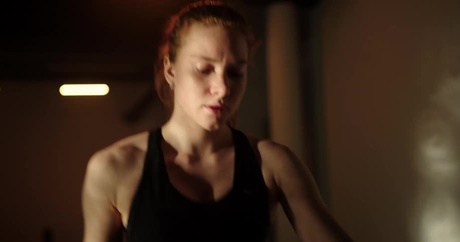Woman with ponytail and black tank top uses cross trainer in gym