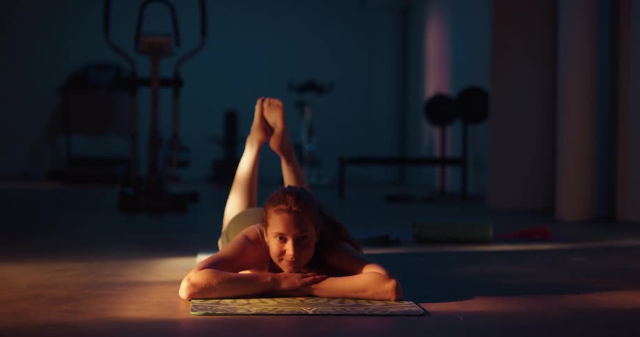 A woman is lying on a rug on the floor relaxing with a smile on her face and her feet in the air