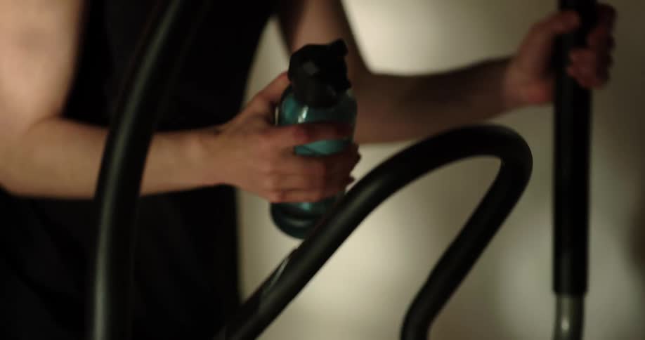 A woman exercising on an elliptical machine and drinking from a water bottle