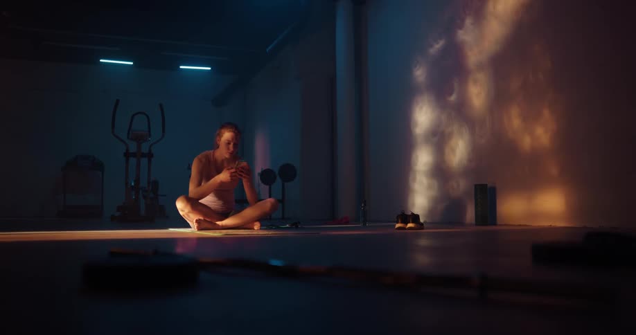 A woman is sitting on the floor with her legs crossed holding her phone