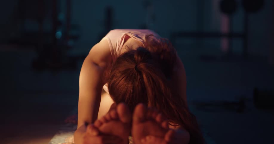 A woman is on a rug on the floor and holding her feet as she bends her head down to her legs