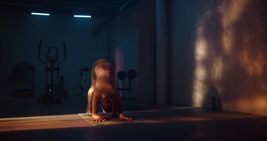 A woman doing yoga on a yoga mat in a dark fitness room