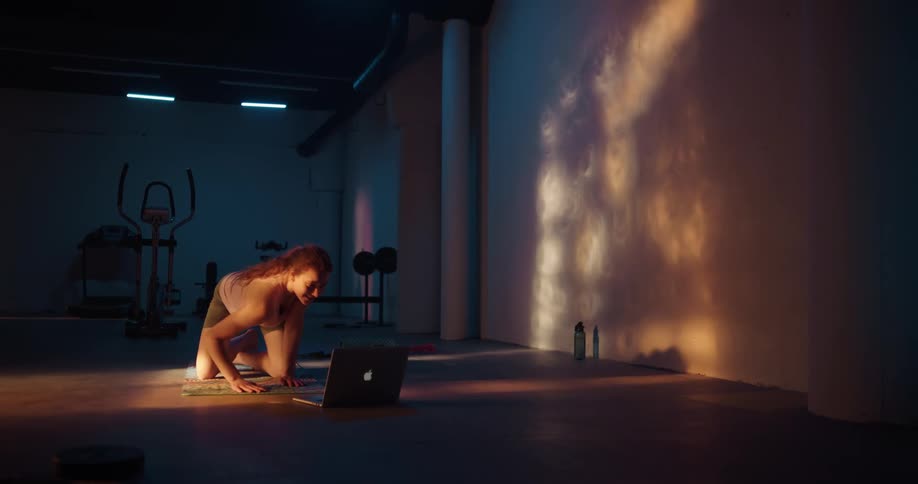 A woman is exercising indoors near a laptop