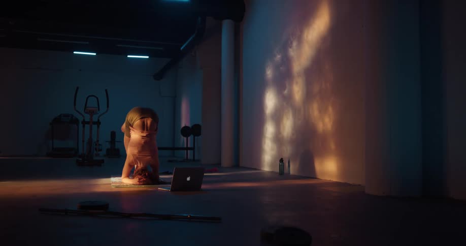 A woman balancing on her head while doing a yoga pose in a fitness room