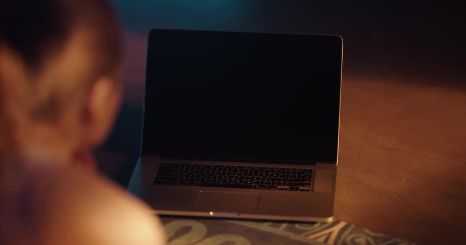 A laptop computer is sitting on the floor and a woman reaches over and pushes a button with her finger