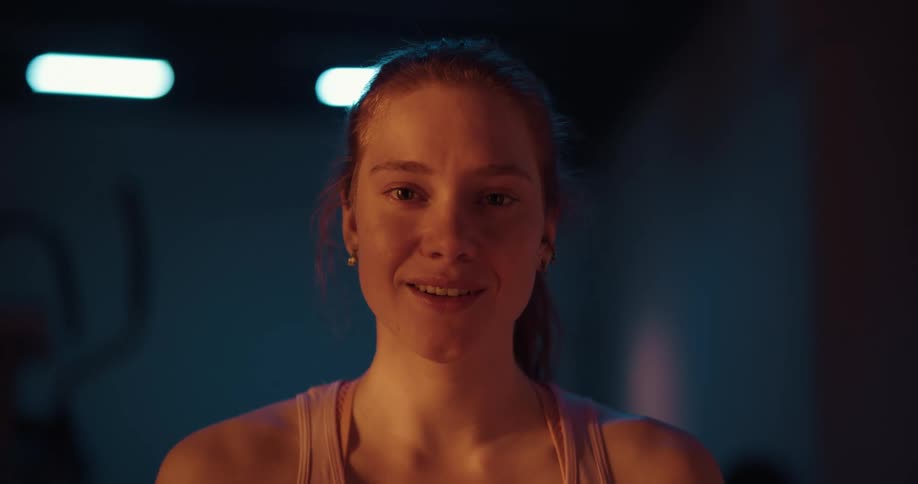 Woman with ponytail and pink top smiles at camera at gym