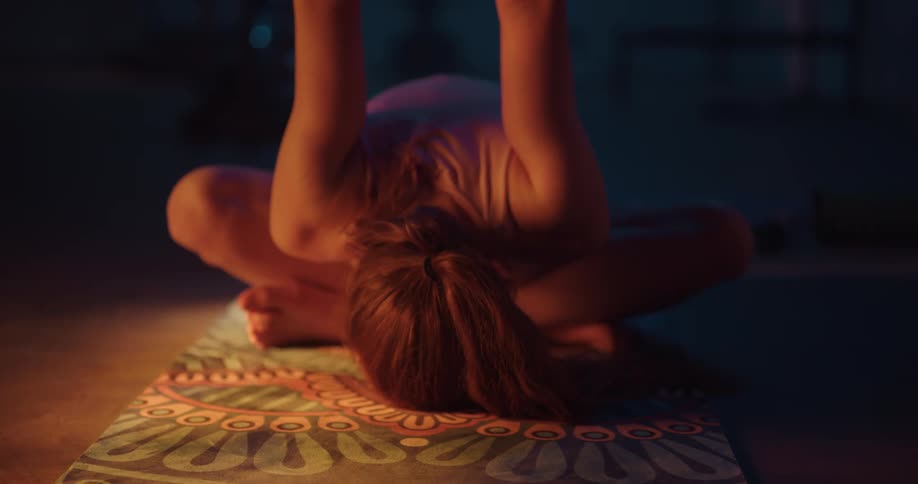 A woman is sitting on a mat with her legs crossed and her arms behind her back as she bends down and touches her face to the floor