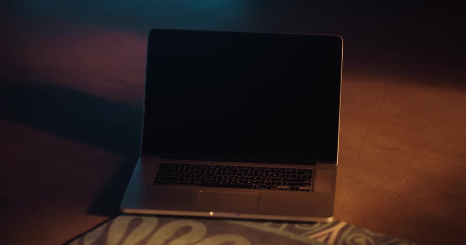 A laptop computer is sitting on the floor and a woman reaches over and pushes a button with her finger