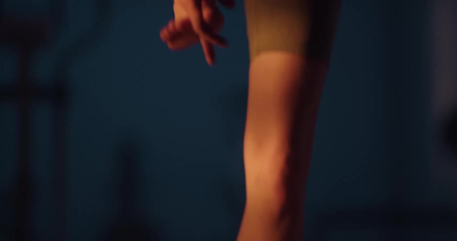 A woman is standing on a mat in her bare feet as she lifts one leg and holds her foot as she stretches out her leg