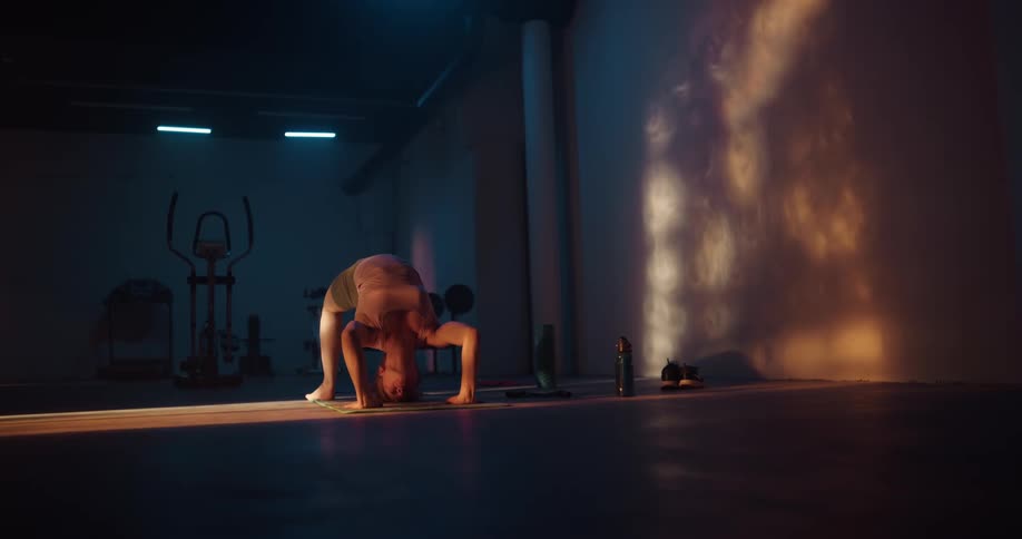 A woman in a back bend position lowers herself to the ground and lifts herself back up in to a back bend as she stretches and then rolls herself in to a ball