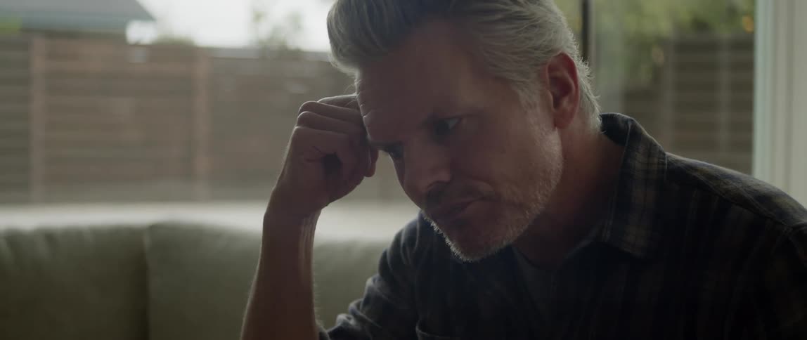 A man is sitting on a couch near a window
