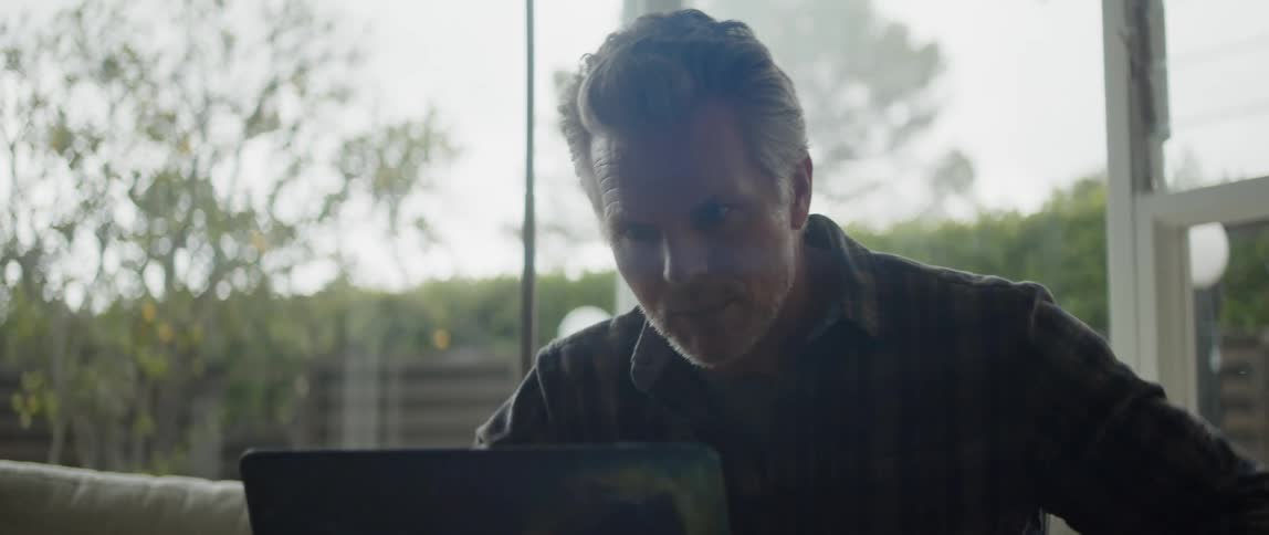 Man sitting on a couch at home talking on a video call through a laptop