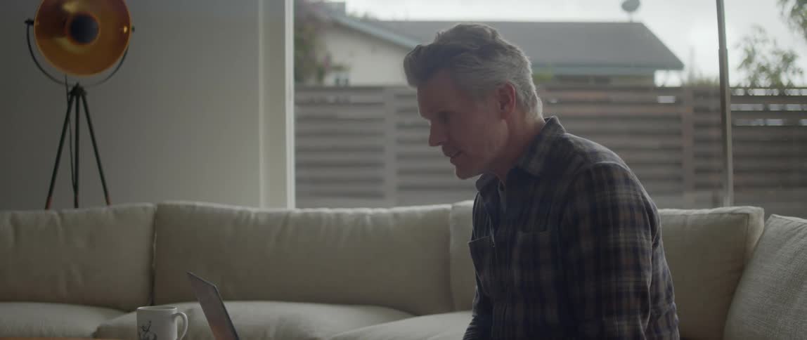 A man sitting on a couch video chatting with someone on his laptop