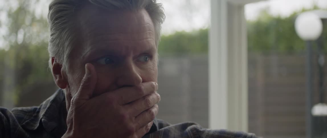 Mature man talking and rubbing his mouth with his hand sitting on a couch at home