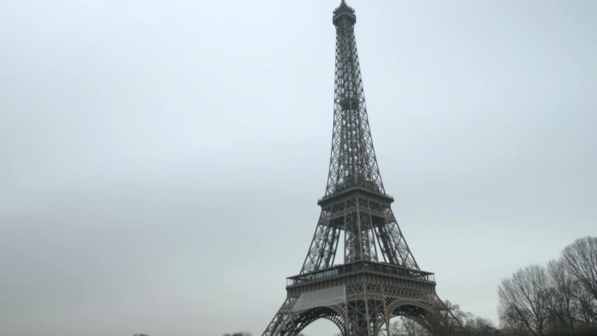 The eiffel tower towers over the city on an overcast day