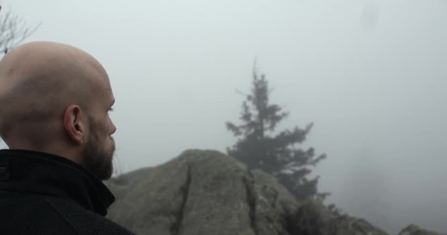 A bald man looks over the edge of the cliff