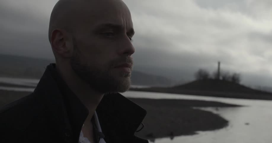 A man is standing by the water and opens his eyes