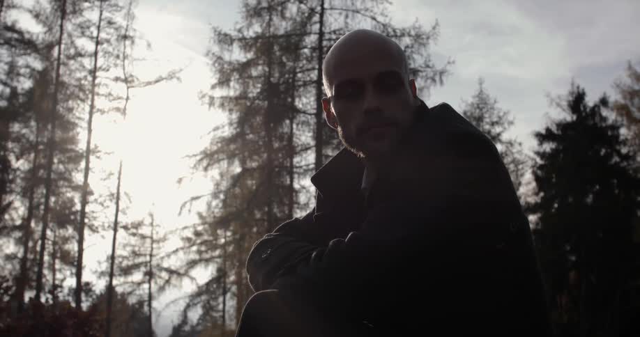 A bald man sits in a forest and looks around