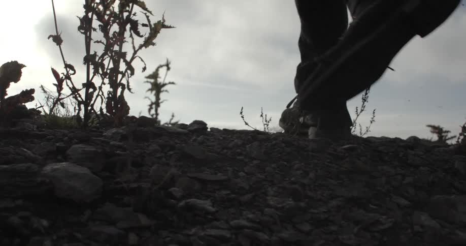 A man walking up a rocky hill at the beach on a cloudy day