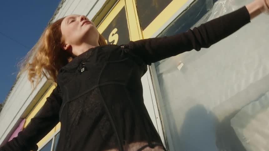 Blonde female dancer wearing black dress dances in front of store