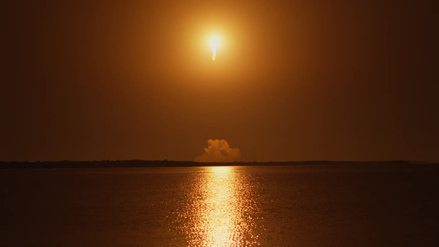 A rocket launches from a coastal area near the water
