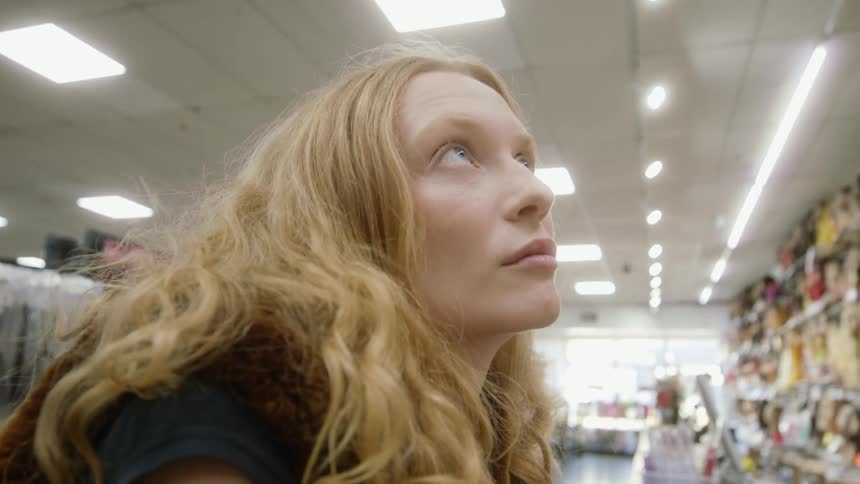 Blonde woman with wavy hair and vest shops at variety store