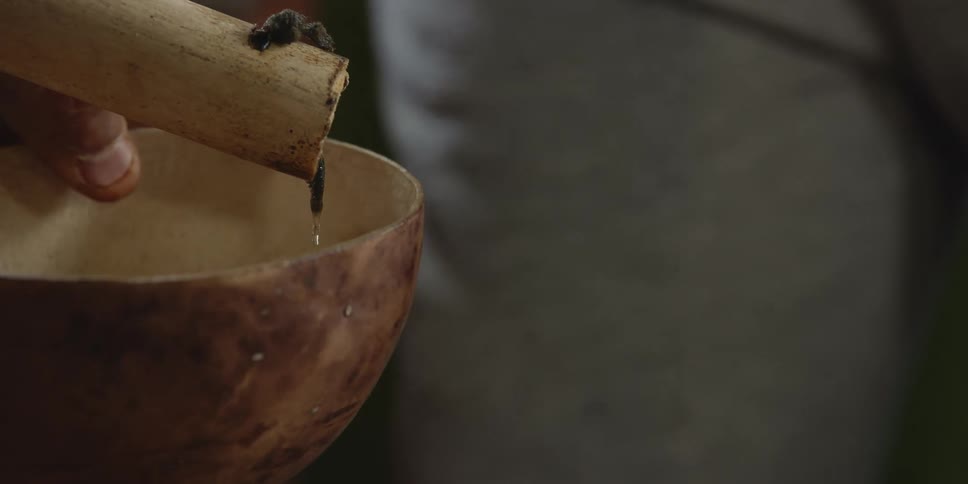 A person collecting water from a wood spigot in a bowl
