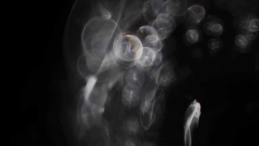 Glowing translucent orbs move across the darkness with wisps of smokey light