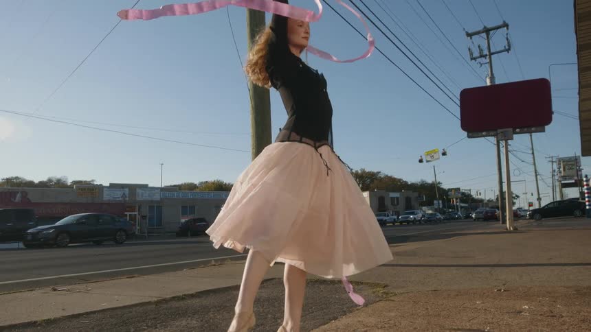 Female ballerina dances on sidewalk between business and busy road