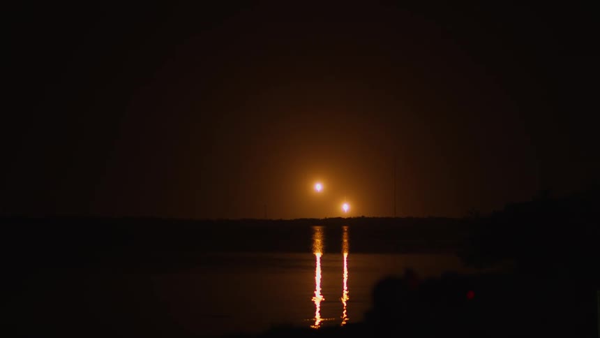 Burning debris falls from the sky after a rocket launch as the light reflects on the water