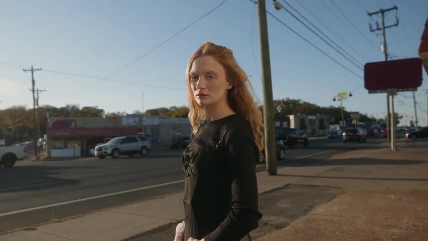 Female dancer with red hair black shirt and white skirt poses for the camera in the street near the highway