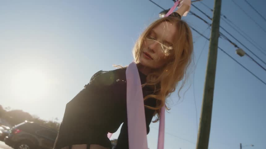 A dancer with a long pink ribbon moves on the side of a road in a town