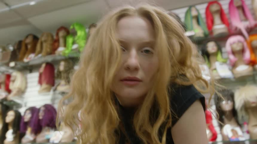 Woman with long hair sits on counter in wig store