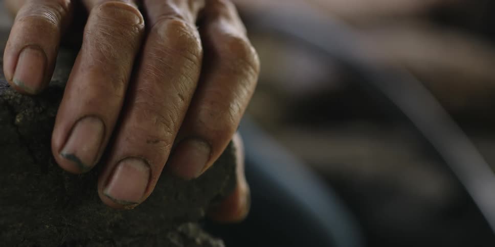 Close up of a mans hand with dirt under his fingernail resting on a rock