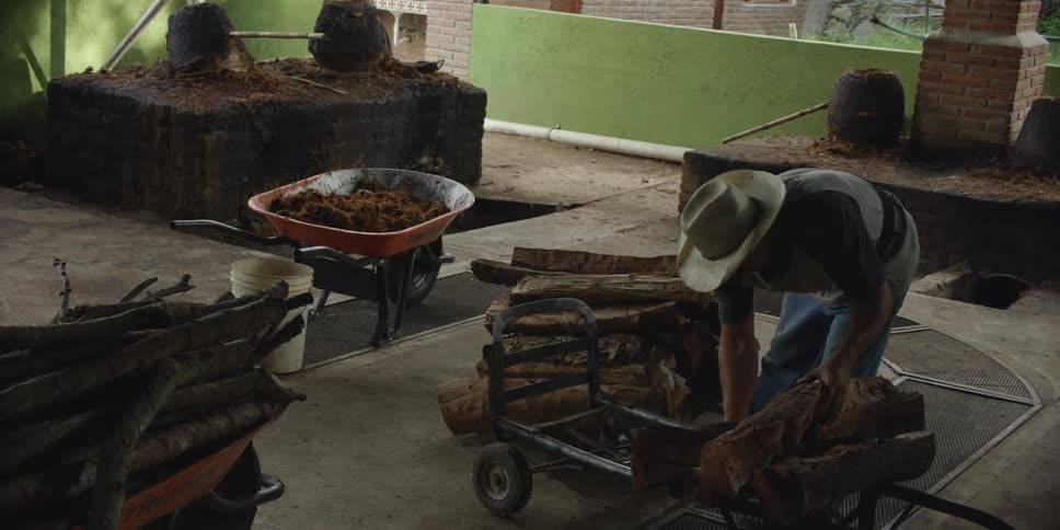 Man stacks logs in structure near multiple firepits and forges