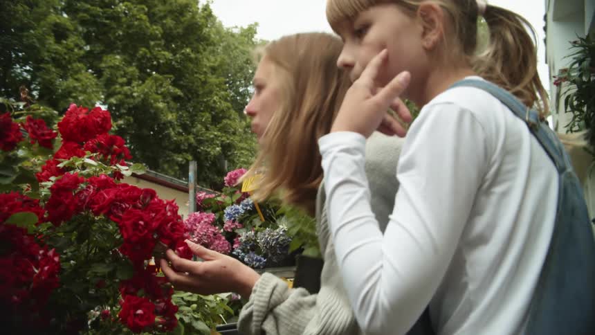 A mom stops to smell a flowering plant as she and her daughter shop in an outdoor garden center
