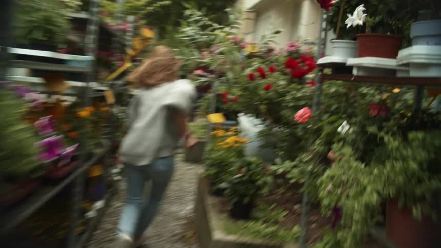 A woman chasing a girl outdoors between shelves with flowers