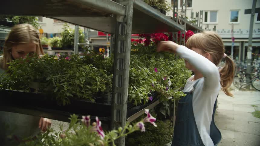 Mother and daughter smelling flower on the outdor shelfs of a store in a small town