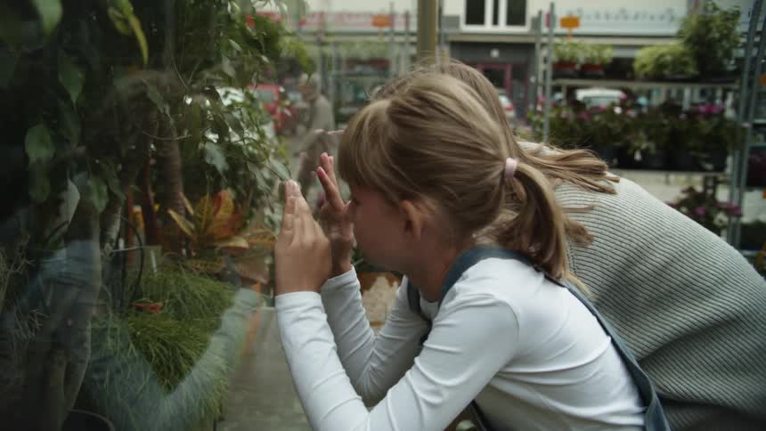 A woman and a girl in a store looking at a window with plants