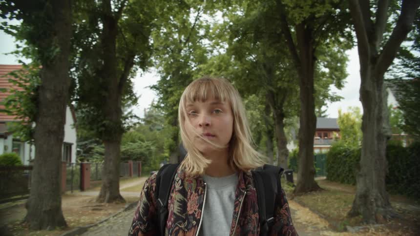 Young blonde woman looking at the camera walking down the street on a calm neighborhood