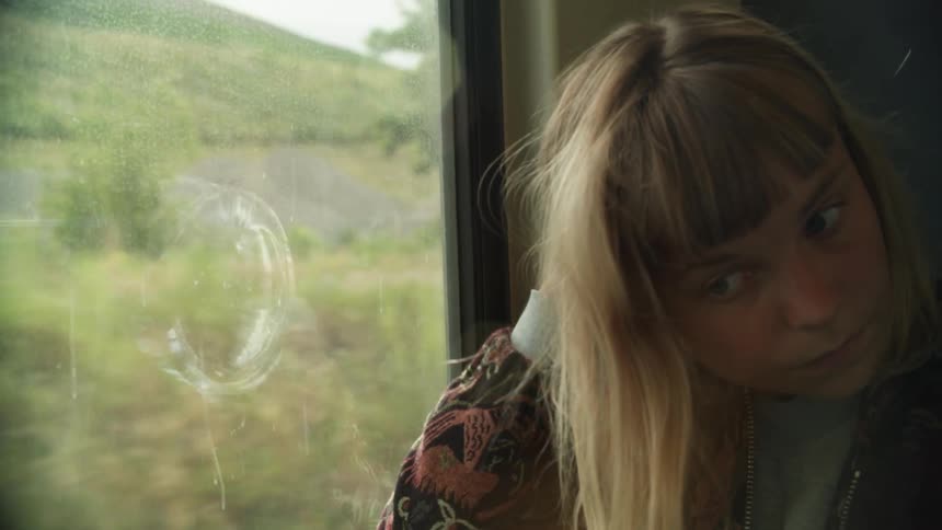 A young woman runs her hand through her hair as she gazes out the window of a train