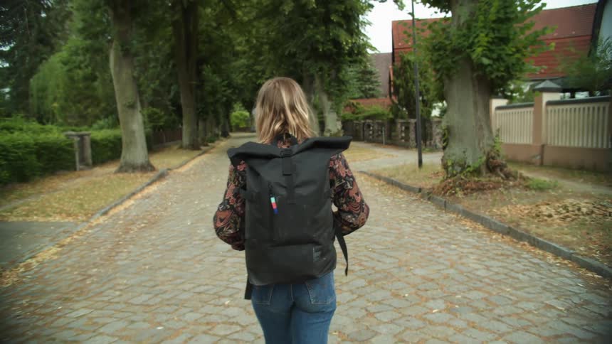 A woman walks alone with a backpack in a small neighborhood