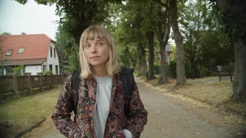 Teenage girl walking down a pathway lined with trees in a neighborhood during the day