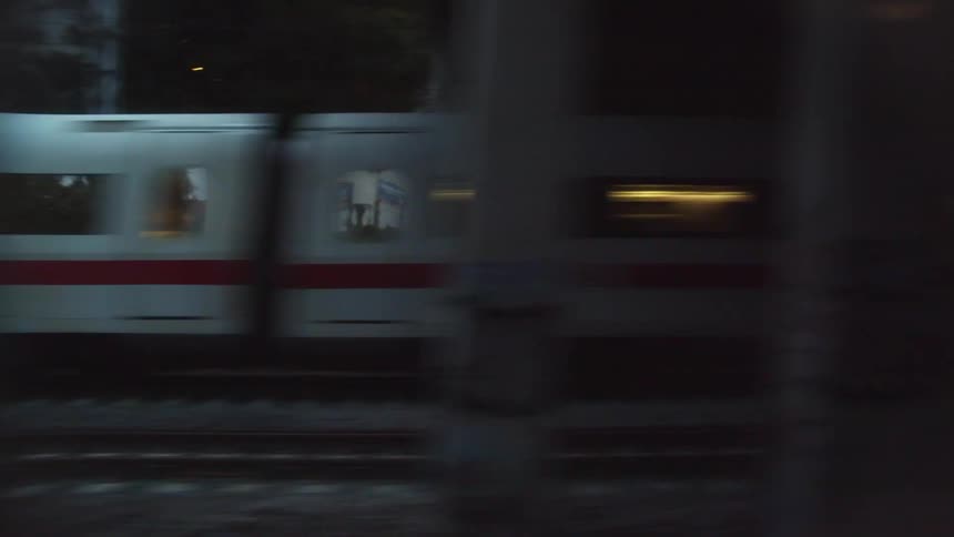 A train running on a train track with buildings the sky and clouds in the background