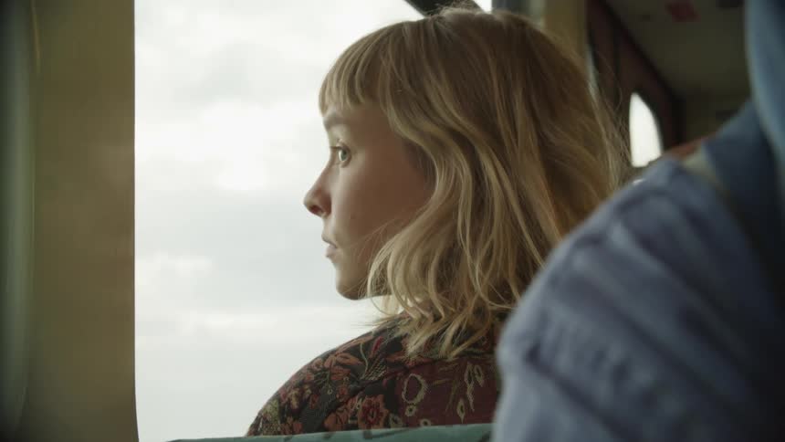 A teenage girl sits on a bus and looks out the window