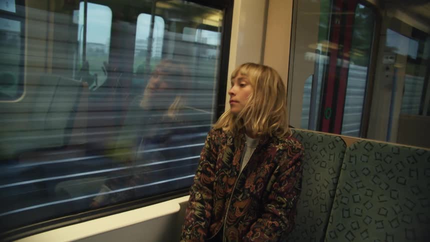 Young woman on a train takes out her backpack and sits in a chair looking out the window