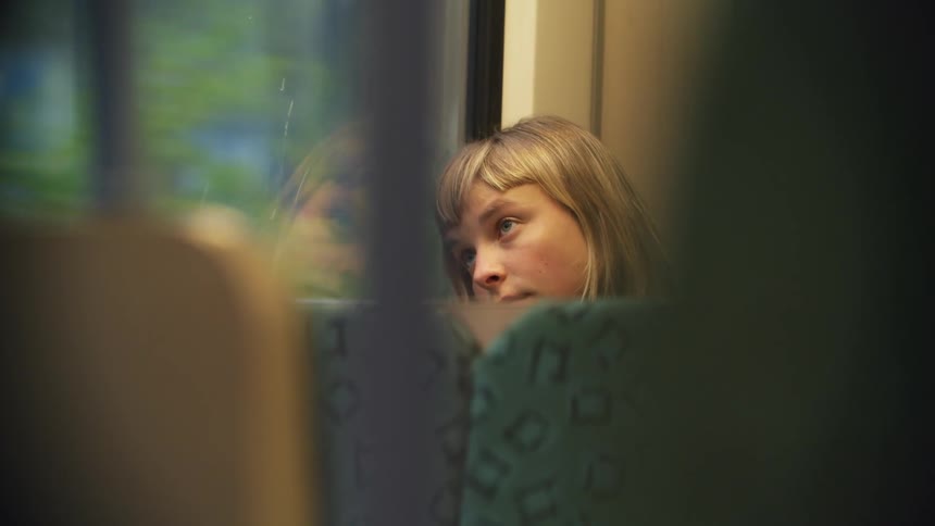 Young woman sitting in a moving train near the window looks outside pensively